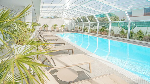 A modern indoor pool area with clear glass walls, sun loungers, and potted plants. - Hotel with swimming pool in Olbia (Olbia)