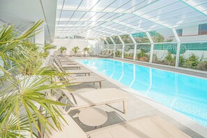 A modern indoor pool area with clear glass walls, sun loungers, and potted plants. - Hotel with swimming pool in Olbia (Olbia)
