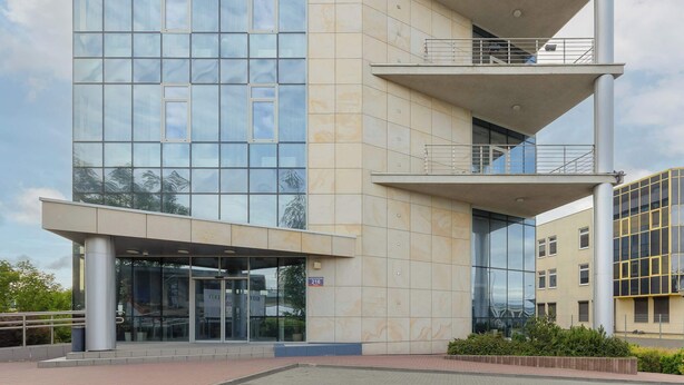 A modern building with a glass facade, a covered entrance, and a visible balcony on the upper floor. - Modern Studio for Two | Parking and Air Conditioning (Warszawa)