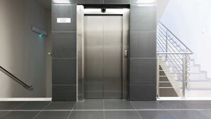 An elevator with a sign indicating 'KLATKA A POZIOM' (floor level) in a modern building with a staircase to the right. - Modern Studio for Two | Parking and Air Conditioning (Warszawa)