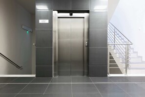 An elevator with a sign indicating 'KLATKA A POZIOM' (floor level) in a modern building with a staircase to the right. - Modern Studio for Two | Parking and Air Conditioning (Warszawa)
