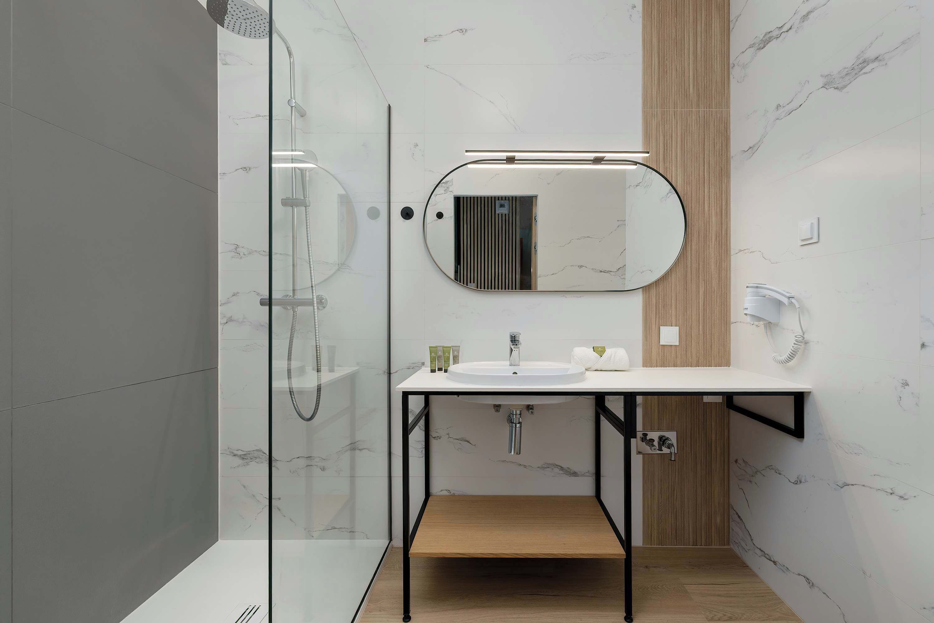 A modern bathroom with a glass shower enclosure, a white sink with a black frame, and a wooden vanity.