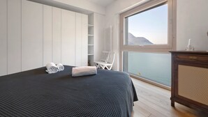 A bedroom with a bed, a chair, a dresser, and a view of the sea. - Dreamy Lakeview Mornings Await! (Orea)