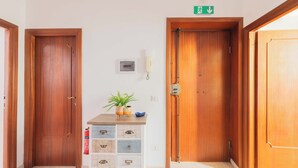 A hallway with wooden doors, a white cabinet with drawers, a potted plant, and a fire extinguisher. - Nosdom Properties - National Street (Roma)