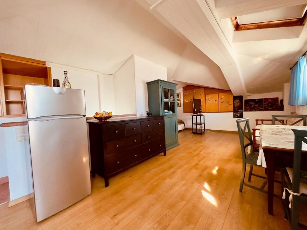 Een kleine keuken met een koelkast, houten kastjes en een eethoek met een tafel en stoelen.