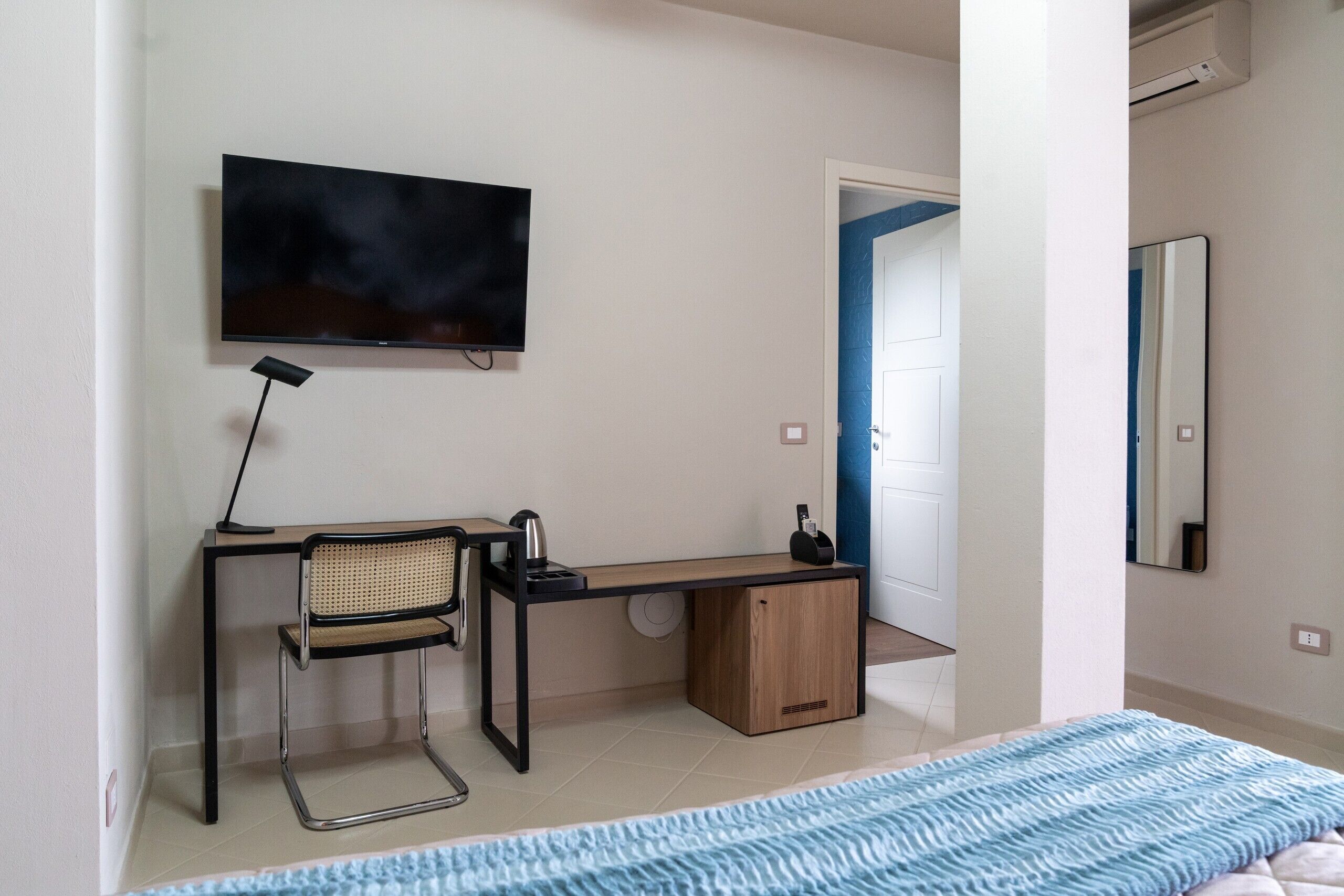 Un dormitorio con cama, un escritorio con silla, televisión y espejo.