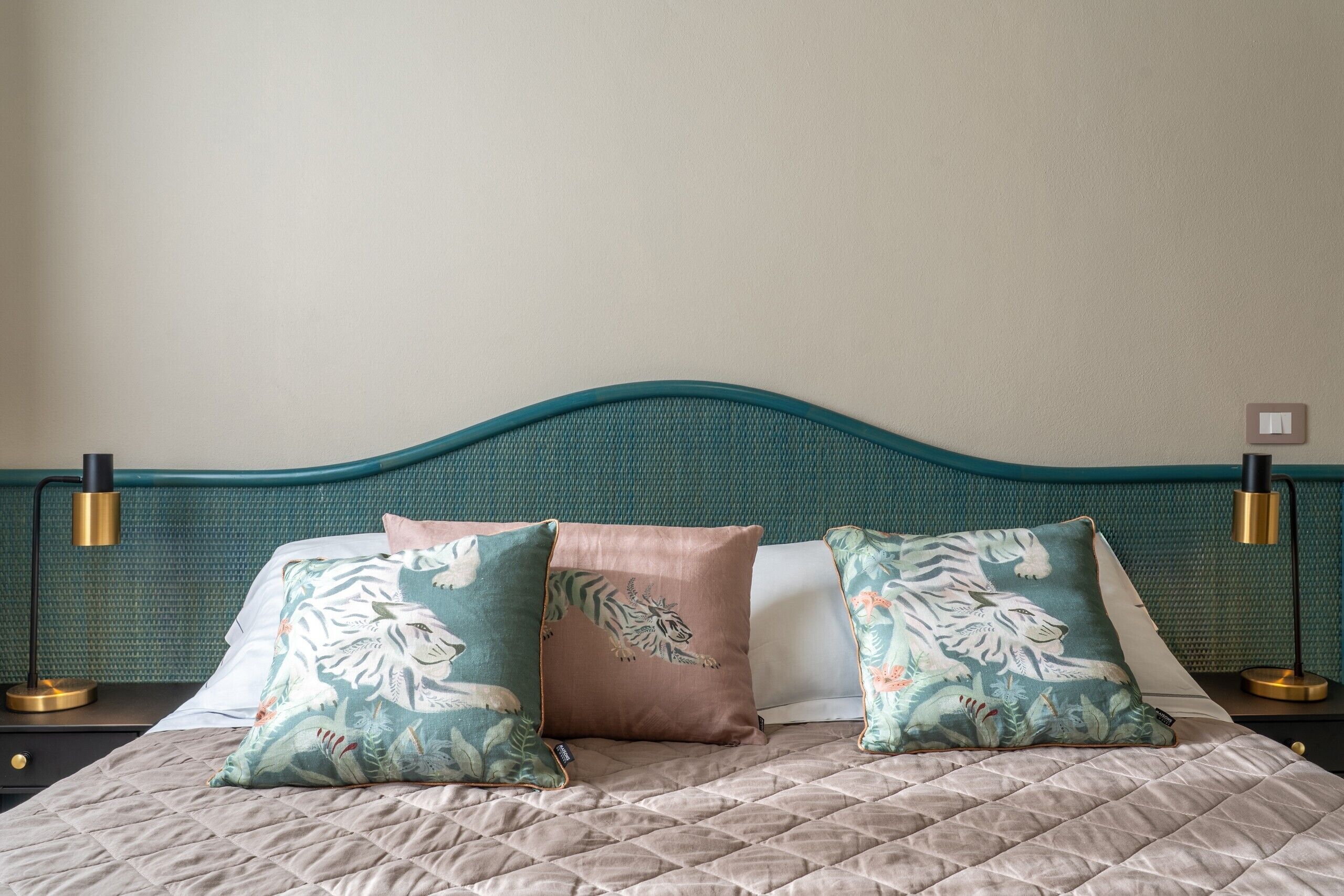 Una cama con una colcha acolchada, dos almohadas con diseños de tigre y flores, y un cabecero color turquesa.
