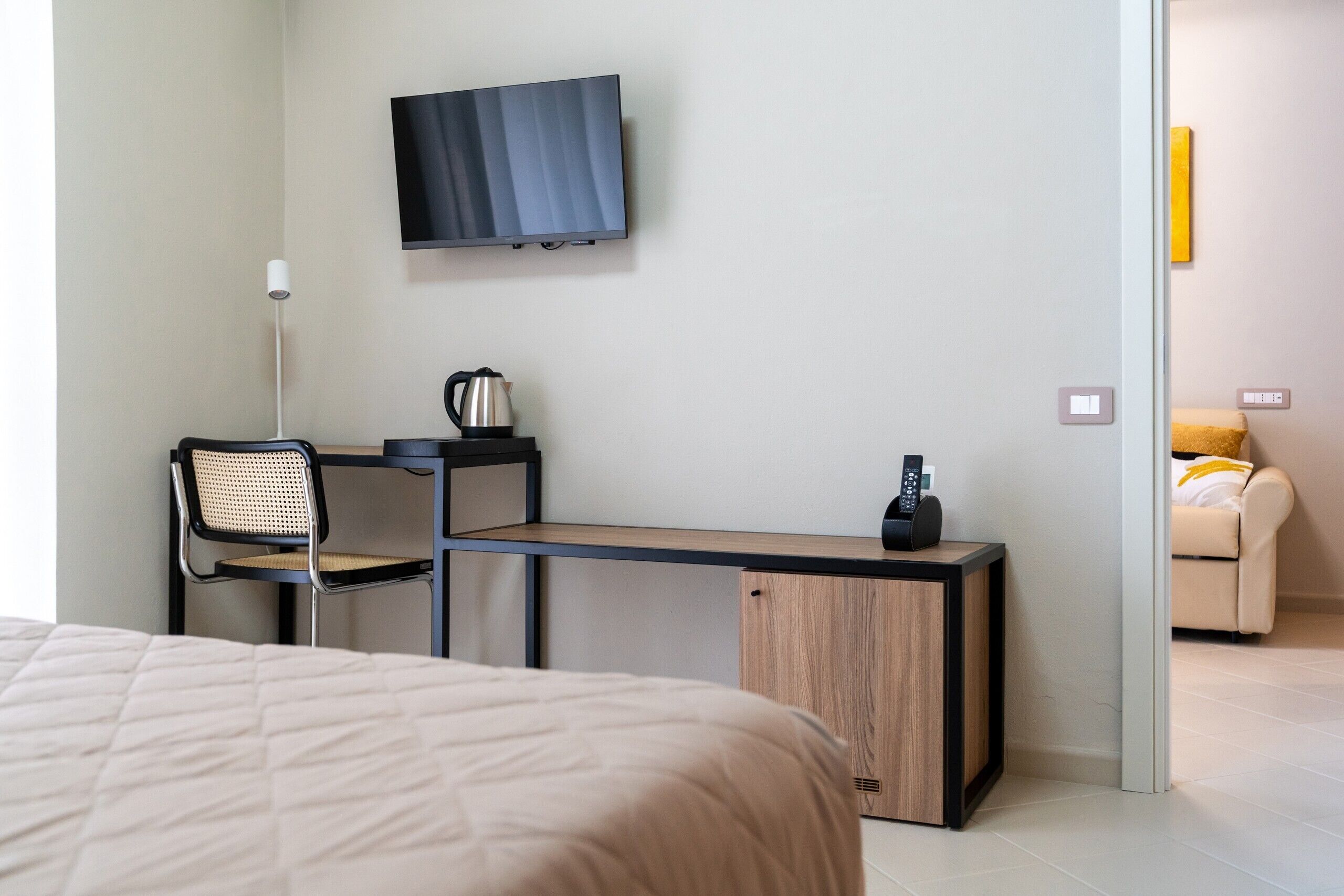 A modern hotel room with a bed, a desk with a chair, a television, a coffee maker, and a small cabinet.