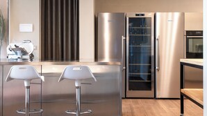 A modern kitchen with stainless steel appliances, a glass door refrigerator, and two white bar stools.
