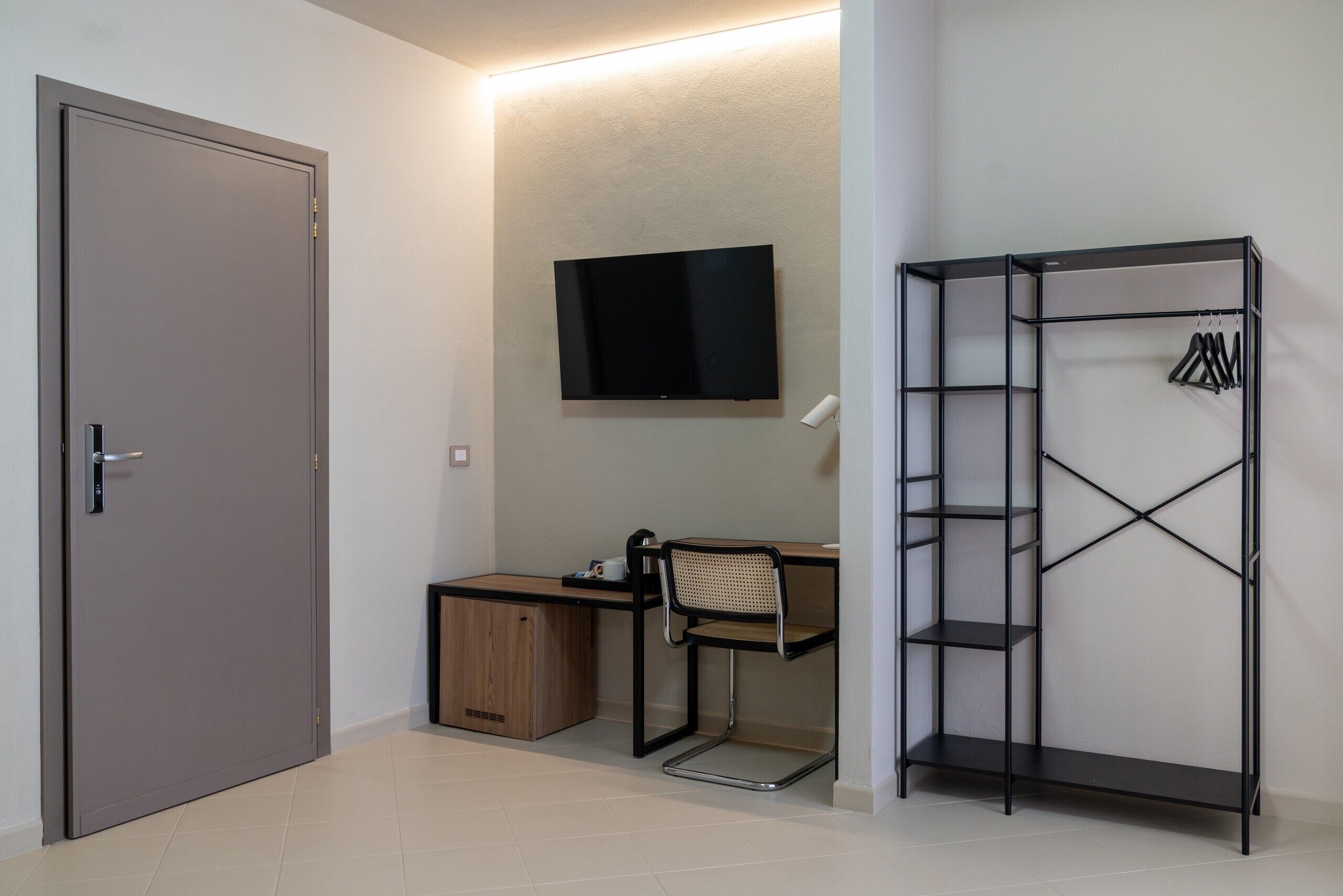 Une petite pièce comprenant un bureau, une chaise, un téléviseur, une armoire et une étagère avec des cintres.
