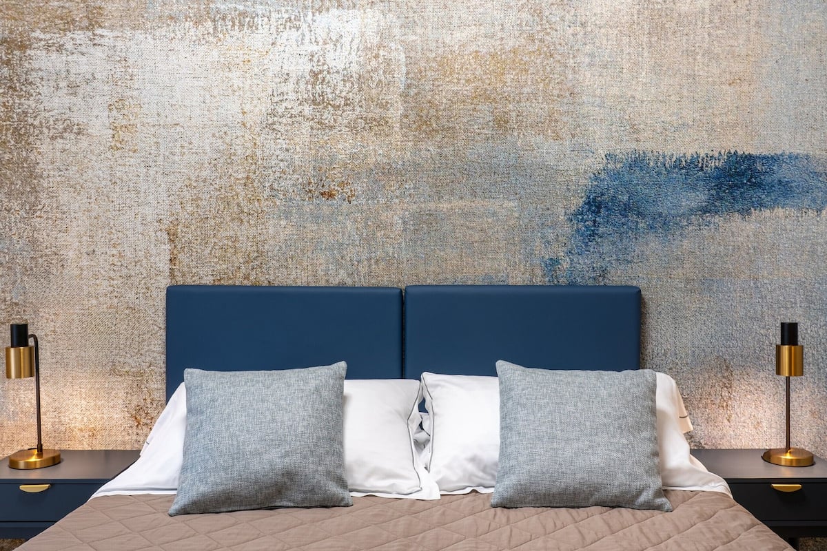 Een bed met een gewatteerd hoofdbord, twee nachtkastjes met lampen, en een gestructureerde muur achter.