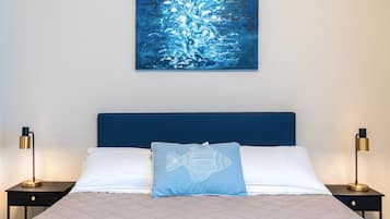 Un letto rifatto con copriletto trapuntato, un cuscino blu con un motivo a pesce e una testiera blu. Ci sono due comodini con lampade su entrambi i lati del letto.
