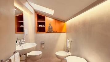 A modern bathroom with two sinks, a toilet, and a bidet. There is a wooden cabinet with shelves and a statue.