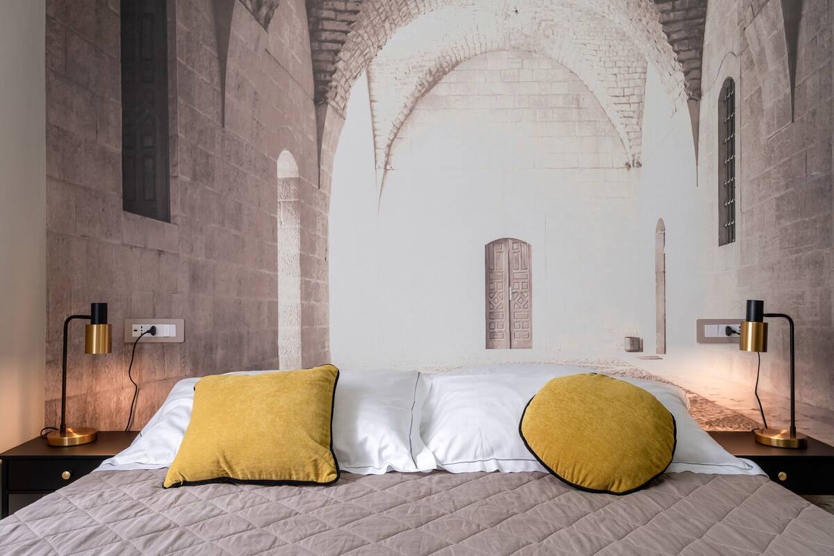 Een slaapkamer met een bed, twee bedlampen en een muurschildering van een gewelfde deuropening.