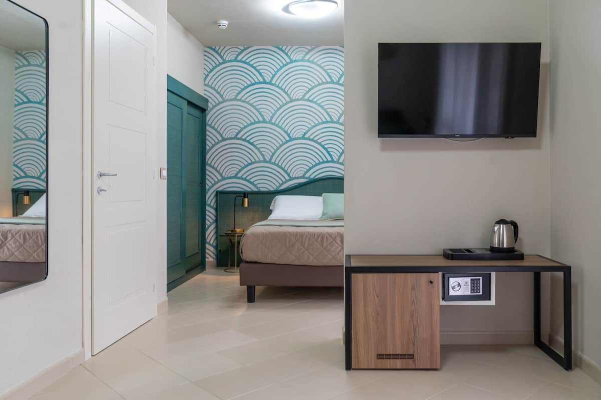 Hotelkamer met een bed, een bureau met koffiezetapparaat, een televisie en een behang met patroon.