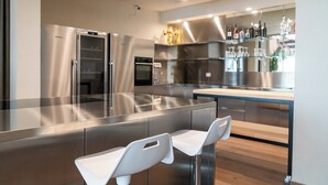 A modern kitchen with stainless steel appliances, a glass dining area, and a bar with bottles.