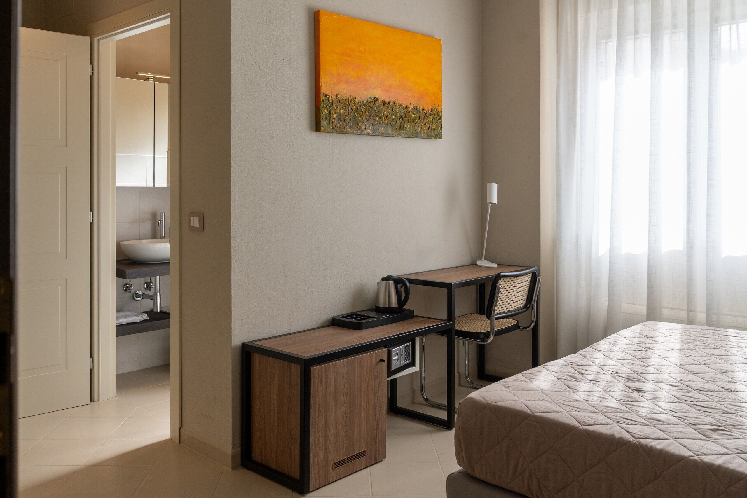 Une chambre d’hôtel avec un lit, un bureau et une chaise, un tableau accroché au mur, et une salle de bain visible à travers une porte ouverte.
