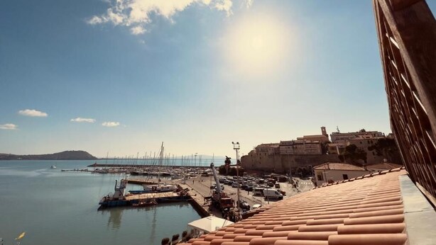 A coastal town with a marina, terracotta-roofed buildings, and a clear sky.