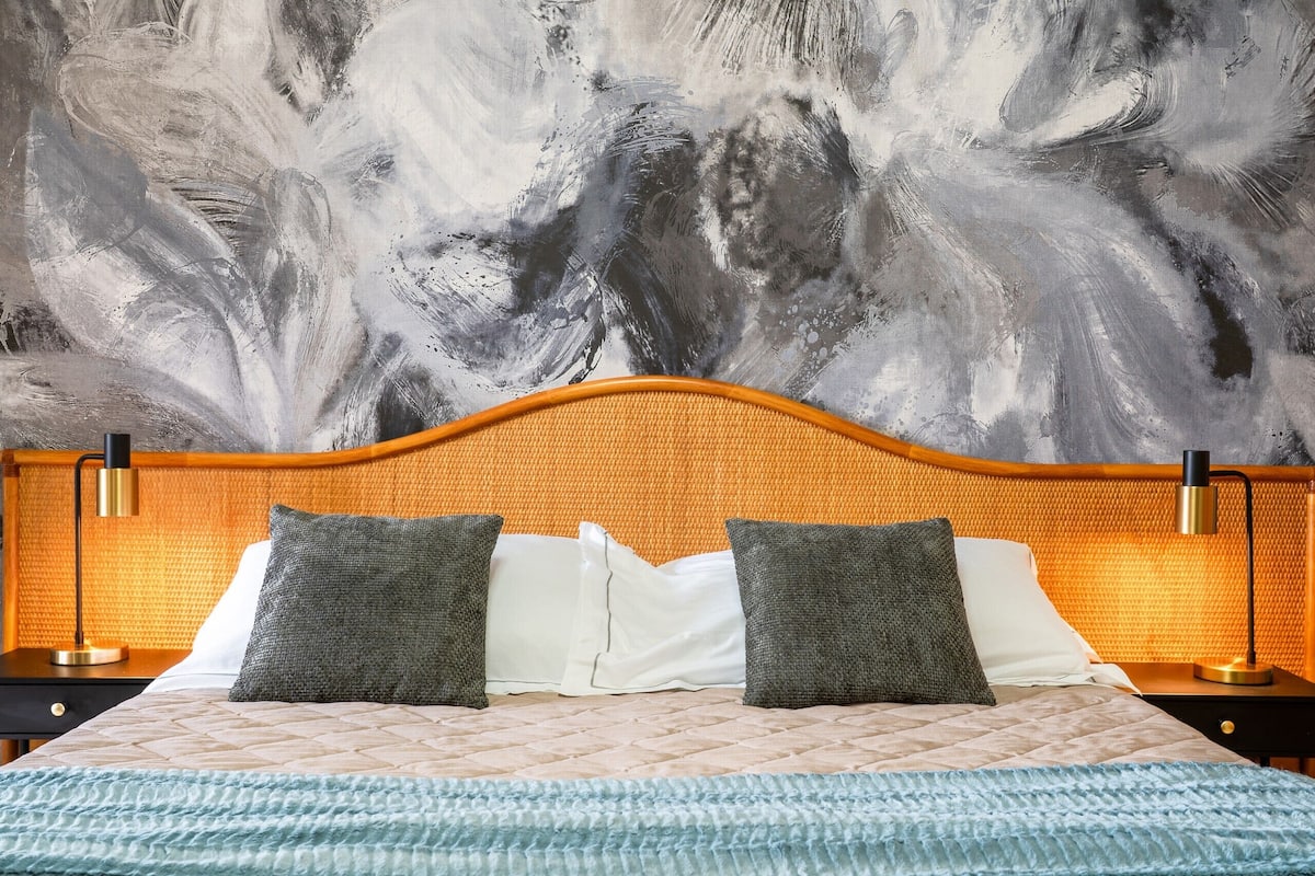 Een bed met een gestoffeerd hoofdbord, twee kussens en een nachtkastje met een lamp.