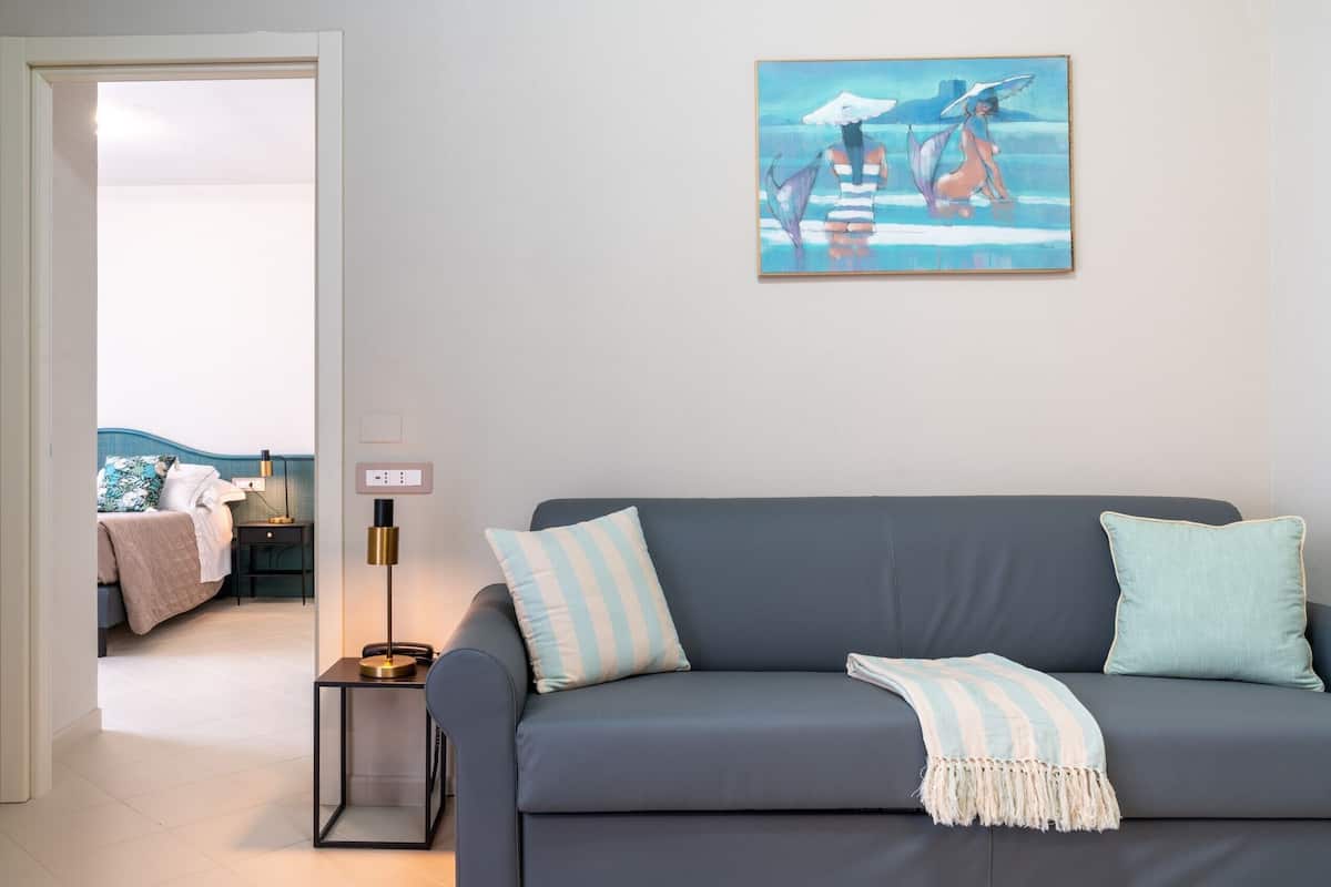 Een moderne woonkamer met een grijze bank, gestreepte kussens en een schilderij van een vrouw in een badpak.