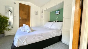 A hotel room with a bed, a green wall, a wooden door, and a potted plant. - Modern Private Guest Suite Near Heathrow Free Parking & Garden (Feltham)