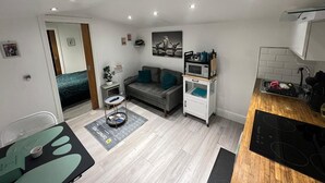A compact living space with a kitchenette, a grey sofa, a small dining table, and a microwave on a white cabinet. - Modern Private Guest Suite Near Heathrow Free Parking & Garden (Feltham)