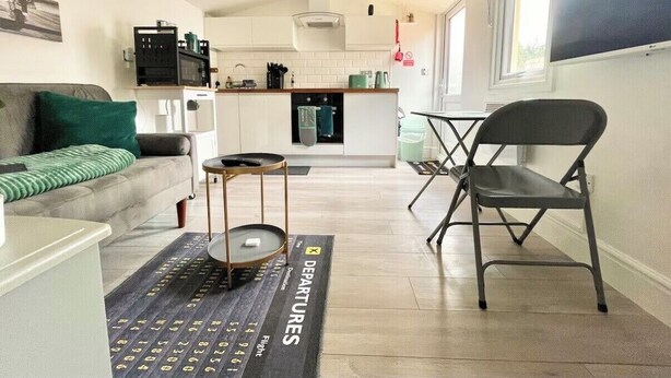 A modern living room with a sofa, a dining table, and a kitchen in the background. - Modern Private Guest Suite Near Heathrow Free Parking & Garden (Feltham)