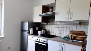 Ett kompakt kök med vita skåp, ett kylskåp i rostfritt stål, en spis och en kaffebryggare.