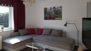Ett vardagsrum med en soffa, ett soffbord i glas, en kristallkrona, en tavla, en tv och en lampa.