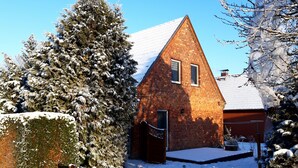 Ett hus byggt av tegel med ett snötäckt tak och ett stort, vintergrönt träd framför.