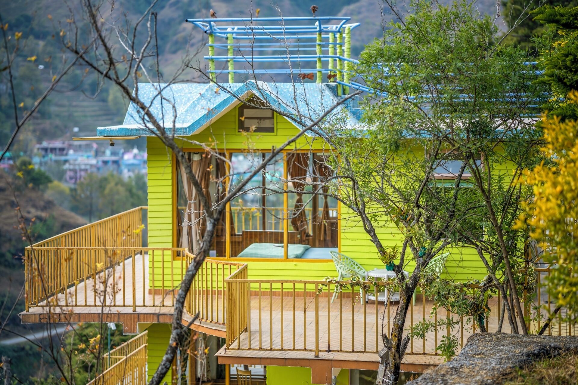 Un edificio amarillo brillante con techo azul, una terraza de madera y una escalera.