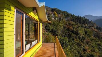 A bright yellow building with large windows and a wooden deck overlooking a mountainous landscape.