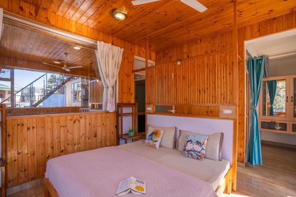 A wooden cabin bedroom with a bed, a window with curtains, a ceiling fan, and a view of the outside.