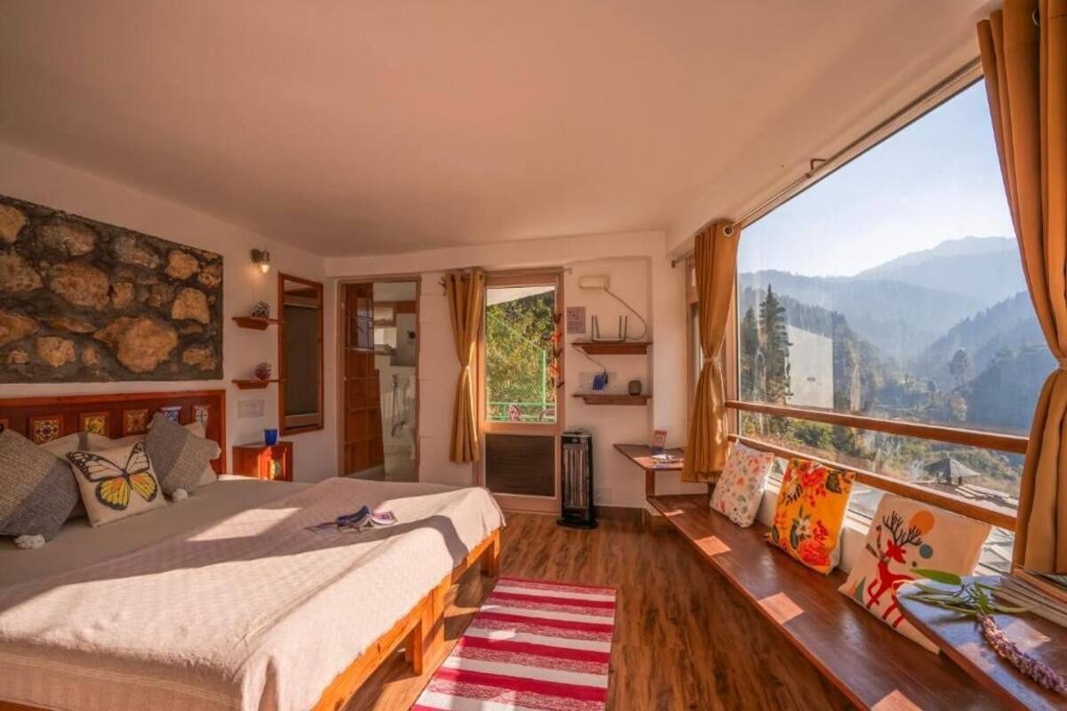 Quarto com uma cama grande, janela com vista para as montanhas, piso de madeira e parede de pedra.