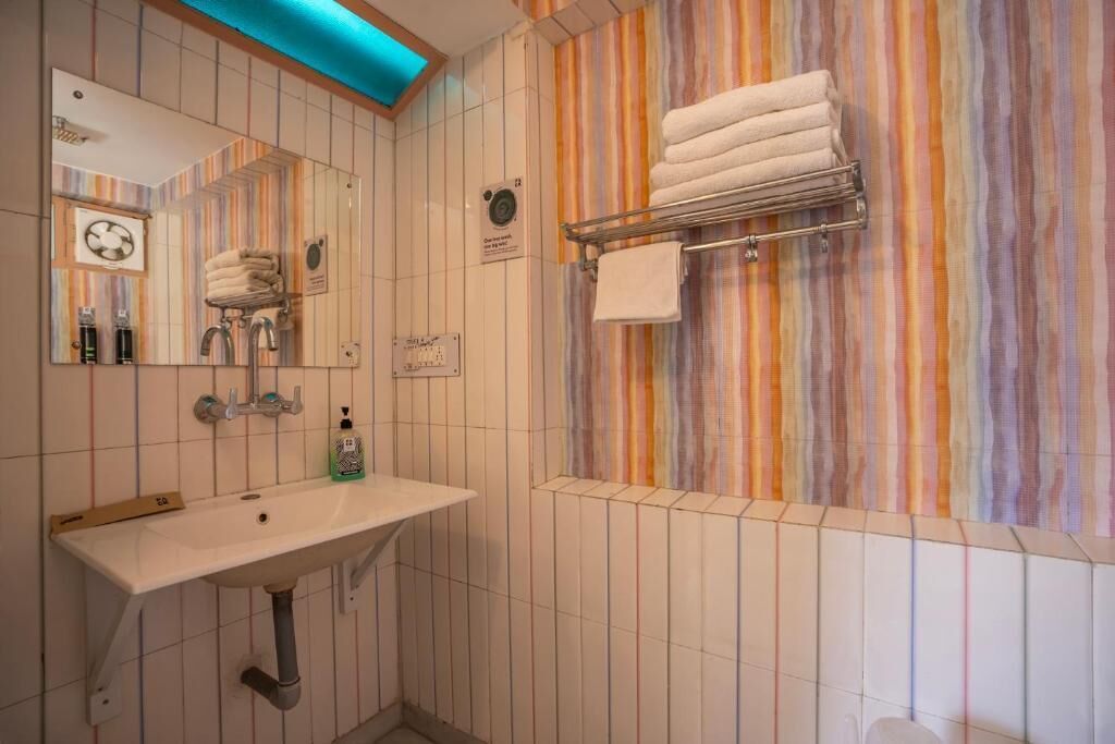 A bathroom with a white sink, a mirror, a towel rack with folded towels, and a striped wall design.