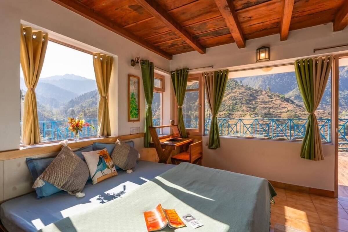 Quarto com cama, escrivaninha e vista para montanhas.