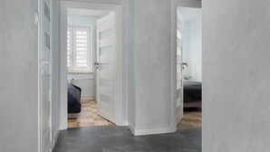 Ein Korridor mit Schachbrettboden, einem Bett mit dunkler Decke und einer Tür zu einem weiteren Raum.
