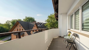 Ein Balkon mit Blick auf angrenzende Häuser, einem kleinen Tisch mit Stühlen und einem Fenster mit Rollläden.