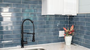 Eine Küche mit Spülbecken aus Edelstahl, weißen Schränken und einer Rückwand aus blauen Fliesen.