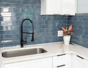 A kitchen with a stainless steel sink, white cabinets, and a backsplash of blue tiles. - Modern & Quiet Oasis, 1 minute walk to the Beach (Madeira Beach)