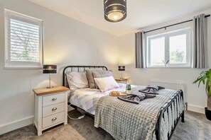 A bedroom with a bed, bedside tables, lamps, a window with curtains, and a potted plant. - Rockford Cottage 3 Bed New Forest House & Garden (Bransgore)