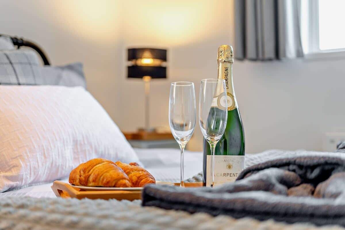 En seng med champagne, to glas og en croissant på et fad.