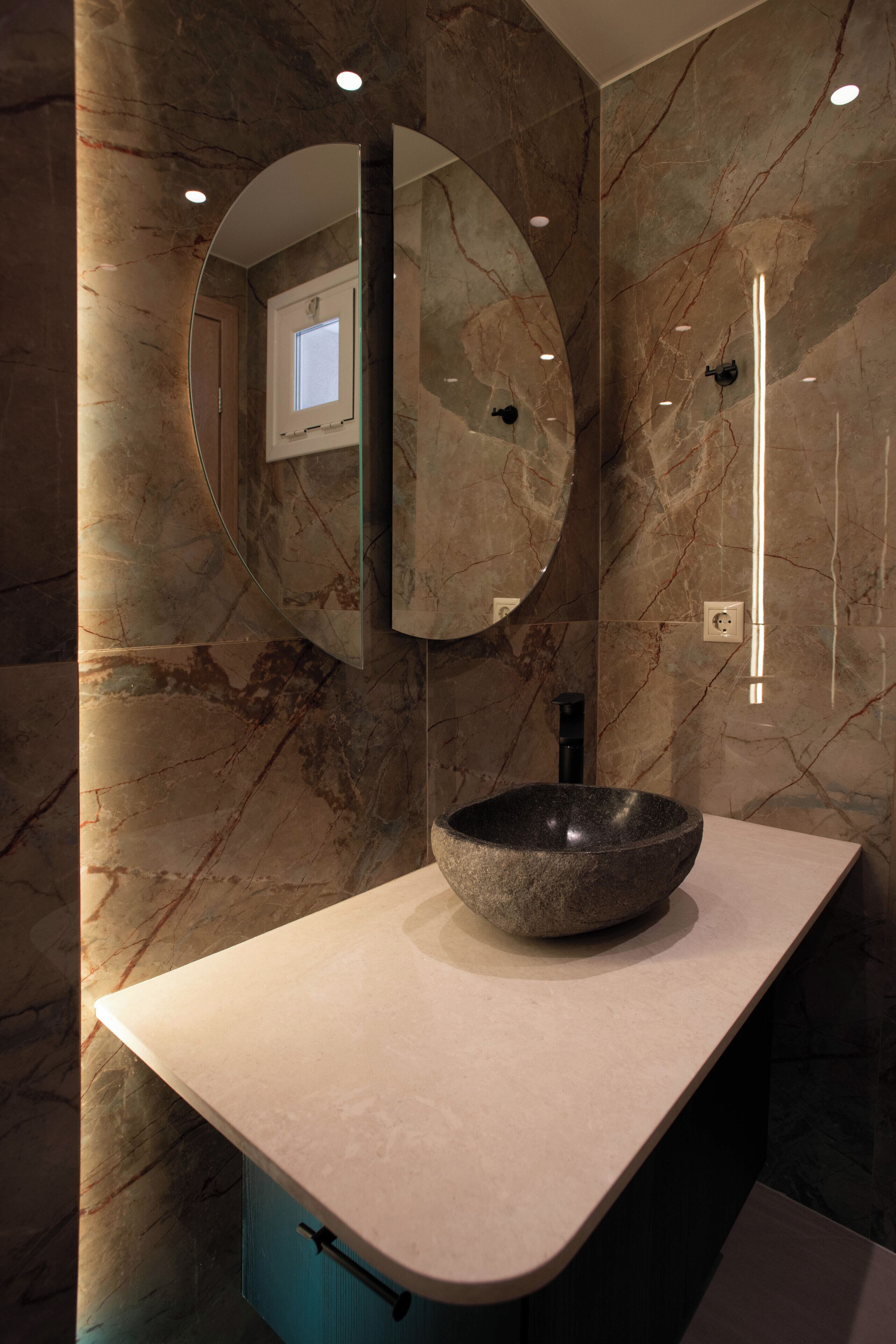 Un bagno con un grande specchio rotondo, un lavabo in pietra e pareti in marmo.