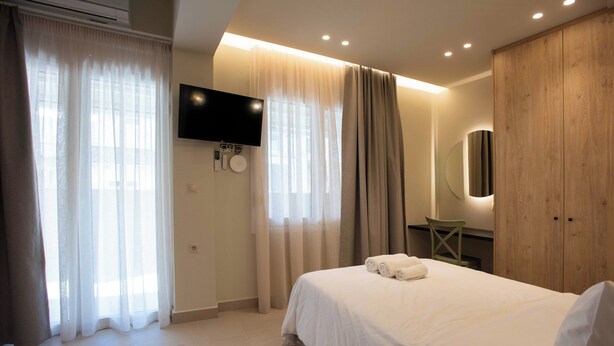 Ein Hotelzimmer mit Bett, Vorhängen, einem an der Wand montierten Fernseher, einem Spiegel und einem Kleiderschrank.
