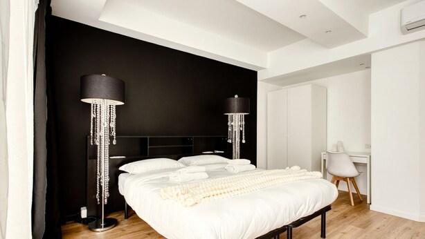Een moderne slaapkamer met een groot bed, twee hoge vloerlampen, een bureau en een stoel.