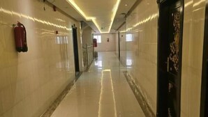 Un pasillo largo e iluminado, con un extintor a la izquierda, una puerta con panel decorativo a la derecha y un piso de baldosas impecables.