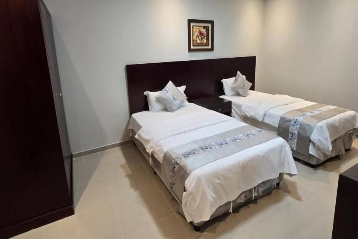 Een hotelkamer met twee bedden, een donker hoofdbord, een ingelijst foto aan de muur en een houten garderobe.