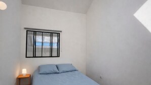 Een slaapkamer met dakraam, een bed met blauw beddengoed, een nachtkastje met lamp en een raam met jaloezieën.
