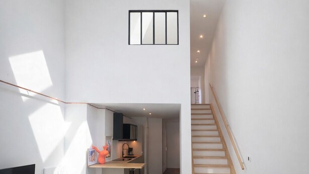 Een ruime woonkamer met dakraam, trap, keuken en zithoek.