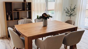 A dining area with a wooden table, six chairs, a vase with flowers, a bookshelf, and a hanging light fixture. - Vacation home Lounis - Apartment 1 (Bützow)